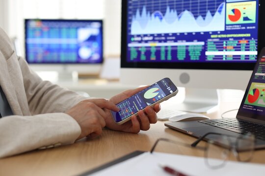 Financial trading specialist using smartphone at wooden desk in office, closeup
