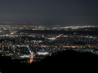 Fototapeta premium Breathtaking aerial nighttime panorama of a Japanese coastal city from a mountain viewpoint. Thousands of city lights illuminate the darkness in a dazzling carpet of light extending to the horizon.