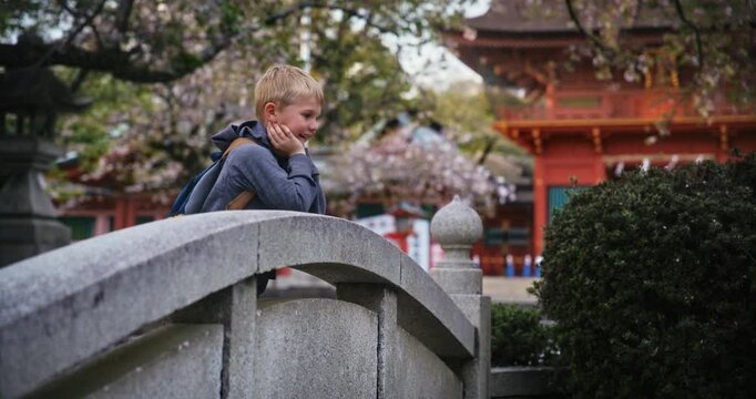 Happy boy staring over stone bridge in Japanese park then nodding at camera - slow motion medium shot