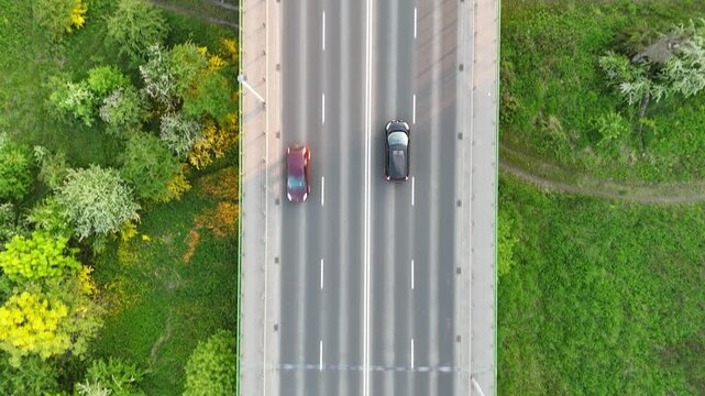 Aerial view of vehicles traveling along a tree-lined road, showcasing the continuous flow of traffic amidst lush greenery and urban elements in a suburban setting. Cars riding at rural route
