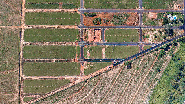 Aerial view of a new housing development with cleared land and roads under construction surrounded by green fields