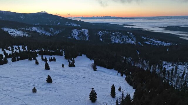 Aerial winter orbit flight over mountain meadow with ski touring tracks before sunrise with misty horizon and Tatra mountains