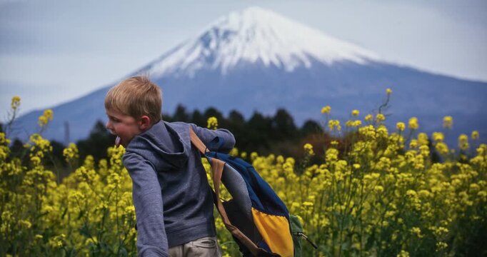 Boy with backpack doing silly dance in front of rapeseed plants and distant Mt. fuji - medium shot