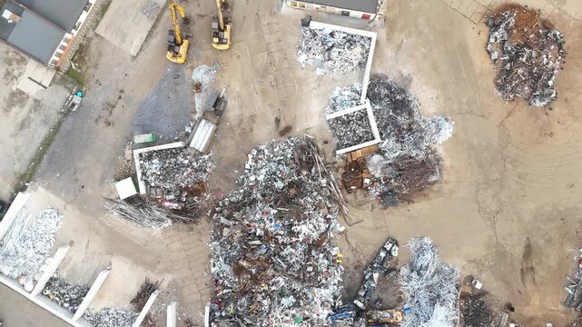 Aerial view of waste sorting and recycling process at a garbage facility, showcasing piles of scrap metal, debris, and machinery in a large outdoor area