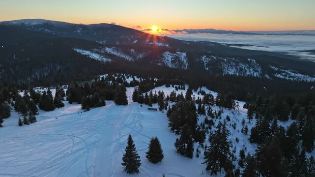 Aerial orbital rotation over snow covered alpine meadow with golden sun rising from behind distant Tatra mountain ridges