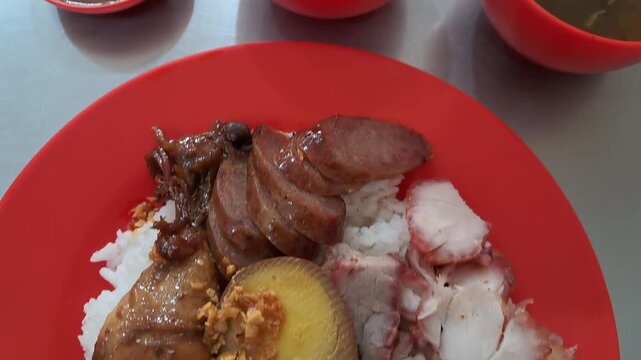 A detailed close up clip of traditional mixed pork rice dish or nasi campur served with side soup bowls.