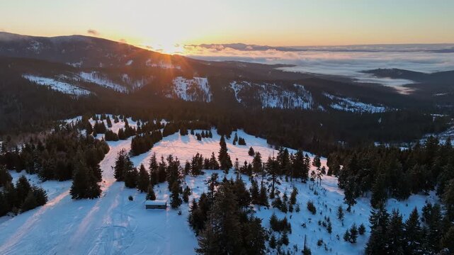 Drone pull back flight over sunlit mountain meadow with tourists silhouettes and misty valley panorama at sunrise