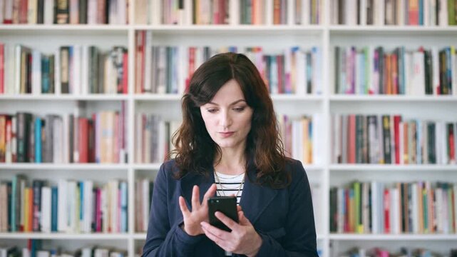 Teacher, education or happy woman with phone in library for academic study, knowledge or information. Female person, professor or scrolling with smile on smartphone for online curriculum or syllabus