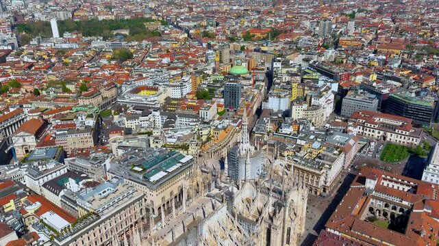 4K aerial drone shot flying over Milan, Italy, offering a close view of the intricate Gothic spires of the Duomo di Milano, the Galleria, and surrounding historic terracotta rooftops.