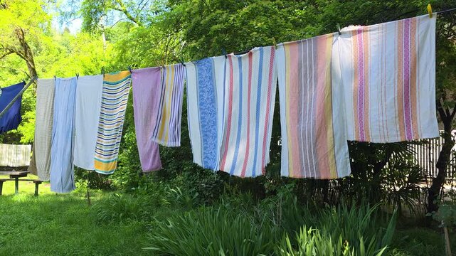 Freshly washed laundry hanging on a clothesline outdoors, drying naturally in the garden, with colorful striped clothes fluttering in the breezy nature