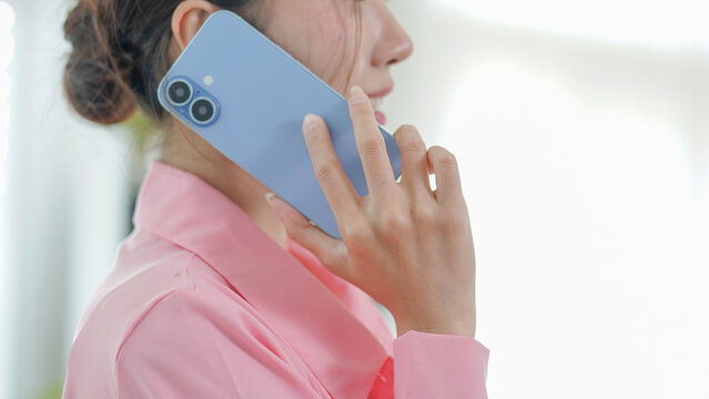 A close-up view of a woman in a pink shirt holding a blue smartphone to her ear during a conversation.