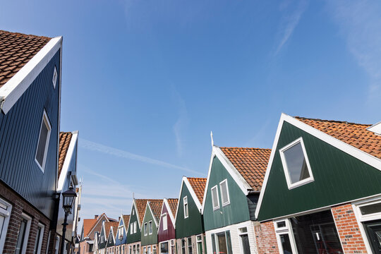 Volendam, Netherlands: A low angle view showing the iconic triangular pointed roofs, colorful wooden facades, and traditional green and blue gables of Dutch houses under a sunny sky.