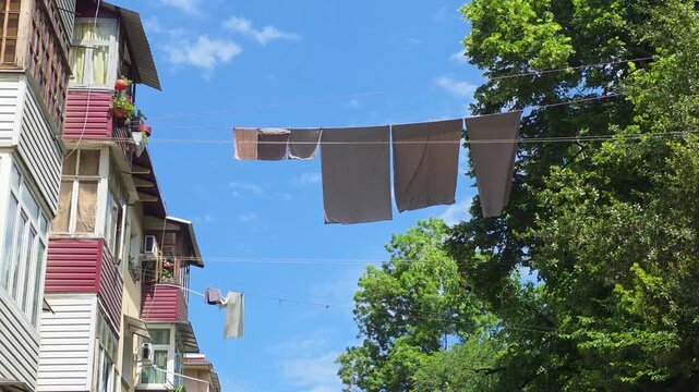 Clotheslines strung between buildings and trees, with laundry drying under a bright blue sky, illustrating daily life and traditional methods in an urban setting