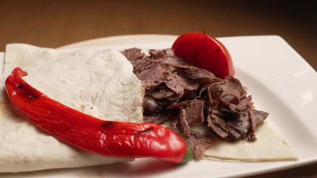 Traditional Turkish dish doner kebab with pita bread, tomato, and grilled pepper rotating on a plate, fa01