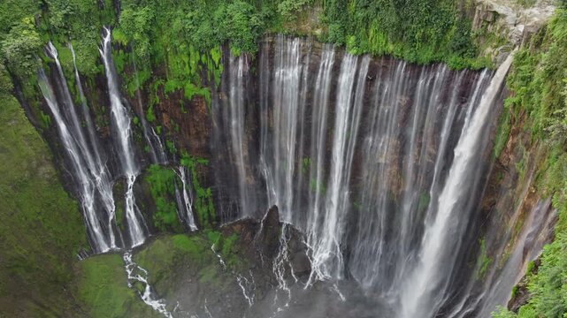 Drone view of Tumpak Sewu Waterfall cascading through a steep canyon surrounded by dense tropical vegetation in East Java, Indonesia.