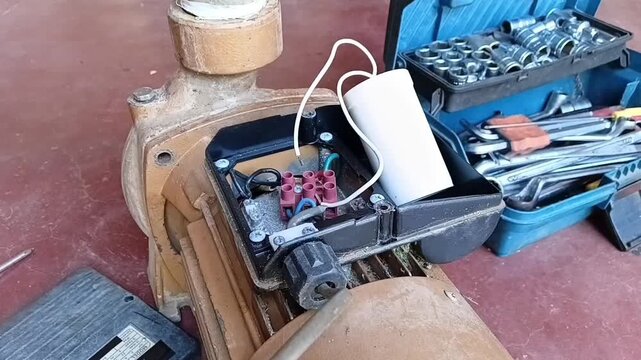 Close-up of a technician removing the white capacitor and disconnecting the winding wires from the terminal block of a water pump.