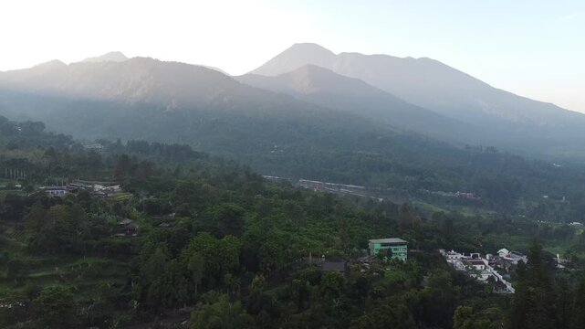 Cinematic drone strafing shot of a peaceful Indonesian mountain landscape and village at sunrise.