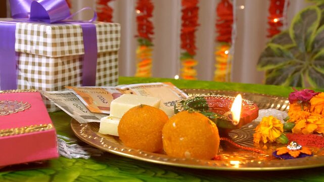 Close-up shot of a decorated thali on the occasion of Raksha Bandhan - Indian festival. Panning right to left shot of Raksha Bandhan puja thali with an elegant rakhi  tikka  sweets  diya  gifts  In...