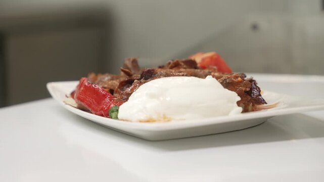Professional chef preparing a plate of İskender kebab by adding a spoonful of fresh yogurt, fa01