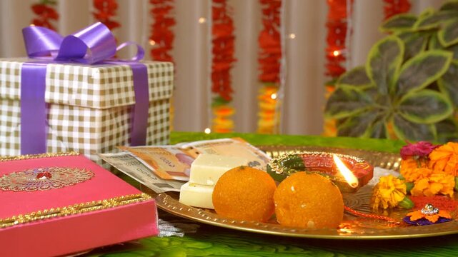 Pan left to right shot of a decorated puja thali - Raksha Bandhan festival. Close up shot of a beautifully decorated thali with laduu  barfi  diya  money  tikka  rice  flower and a handmade rakhi -...