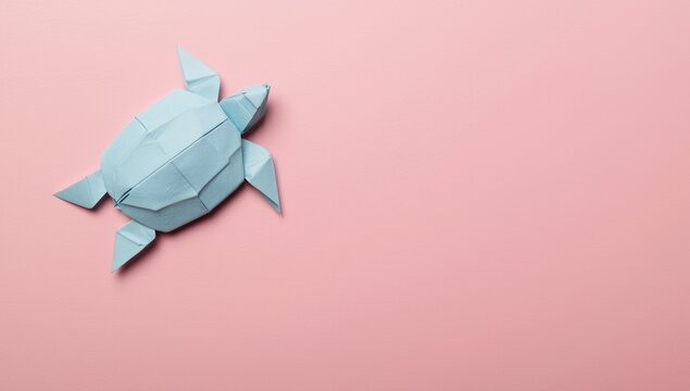 Photo from above of a paper turtle with handmade light blue folds in origami on a pink base