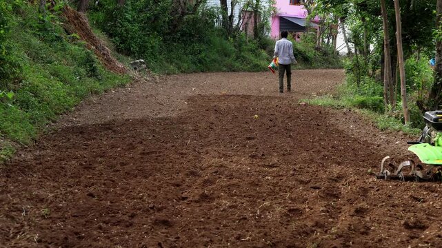 Closeup video of an Indian farmer scattering seeds by hand across an agricultural field before plowing with a power tiller during summer season in Himachal Pradesh, India.