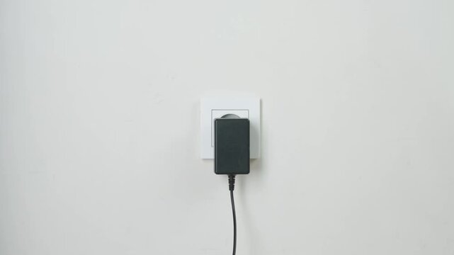 Hand Plugging Power Cable Into White Electrical Socket