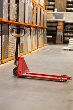 Red manual pallet jack parked in empty warehouse aisle