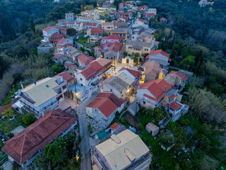 Fototapeta premium Aerial view of the traditional village of Antipernoi with illuminated streets and red tiled roofs during evening twilight on Corfu Island, Greece.