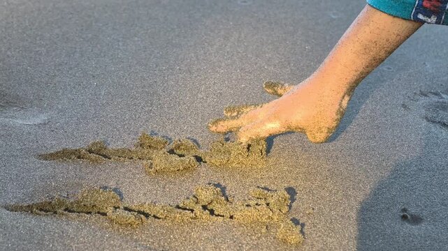 A child hand drawing lines on wet beach sand, shortly washed away by a gentle oncoming ocean wave. Conceptual video for fleeting moments.
