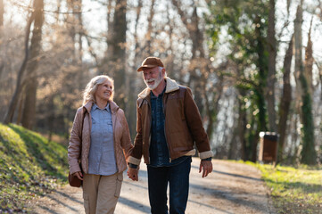 Fototapeta premium Happy senior couple enjoying a conversation during a walk in the park. Active retirement lifestyle, companionship, friendship and healthy aging in a peaceful outdoor setting