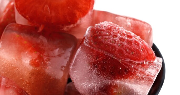 Frozen strawberries in ice cubes with melting water and reflections
