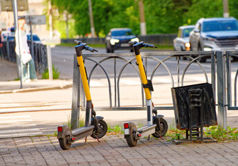 Electric scooters standing by a metal fence on a sunny urban street. Modern public transportation, mobility and city life concept with moving traffic in the background. Photo © slexp880