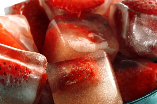 Frozen strawberries in ice cubes with melting water and reflections
