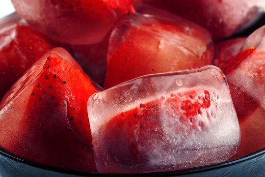 Frozen strawberries in ice cubes with melting water and reflections