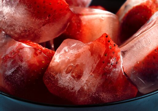 Frozen strawberries in ice cubes with melting water and reflections