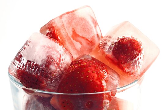 Frozen strawberries in ice cubes with melting water and reflections
