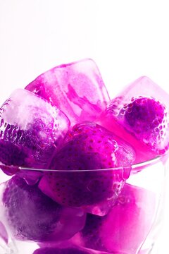 Frozen strawberries in ice cubes with melting water and reflections