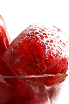 Frozen strawberries in ice cubes with melting water and reflections