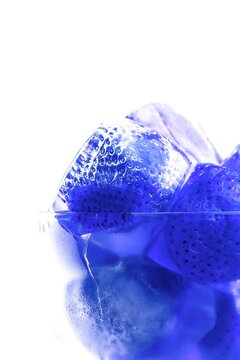 Frozen strawberries in ice cubes with melting water and reflections