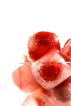 Frozen strawberries in ice cubes with melting water and reflections