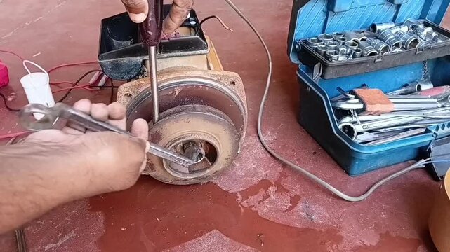 Close-up of a mechanic using a wrench to remove the impeller lock nut from the rotor shaft of a damaged electric water pump.
