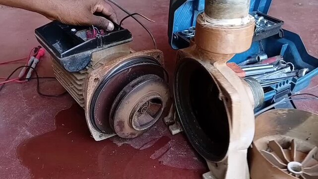 A technician separating the water pump casing and trying to spin the impeller, demonstrating jammed bearings due to flood damage.