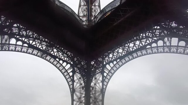 Symmetrical low-angle view of the Eiffel Tower's iron lattice structure on a cloudy day in Paris, eb01