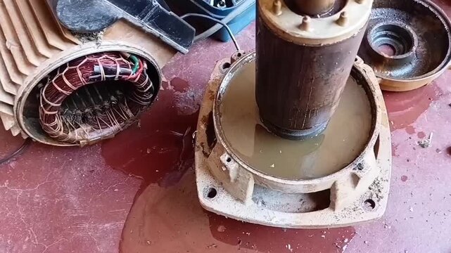 Close-up of the fully dismantled electric motor parts, showing the dripping stator coil, dirty rotor, and water-filled front endshield.
