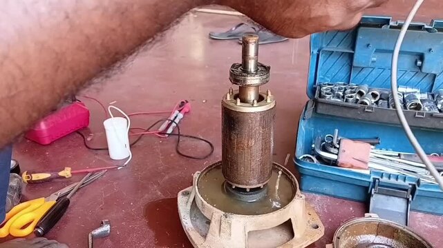 A mechanic pulling out the stator coil from the motor body, with dirty muddy water dripping from the windings and filling the front endshield.