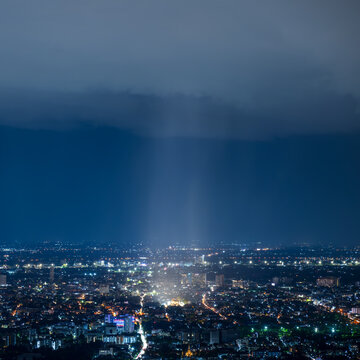 Dramatic night landscape view of Chiang Mai cityscape featuring a rain shaft pouring directly over the ancient pagoda of Wat Chedi Luang temple 