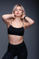 Obraz premium Athletic woman with blonde hair in black sportswear posing against a dark background