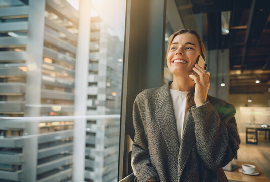 Happy Caucasian female professional smiles warmly during a phone call in a modern office with bright natural lighting and optimistic vibe
