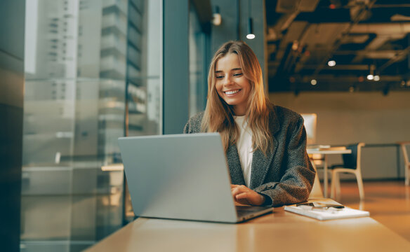 Cheerful Caucasian female entrepreneur working on a laptop under warm natural light with a positive and authentic vibe